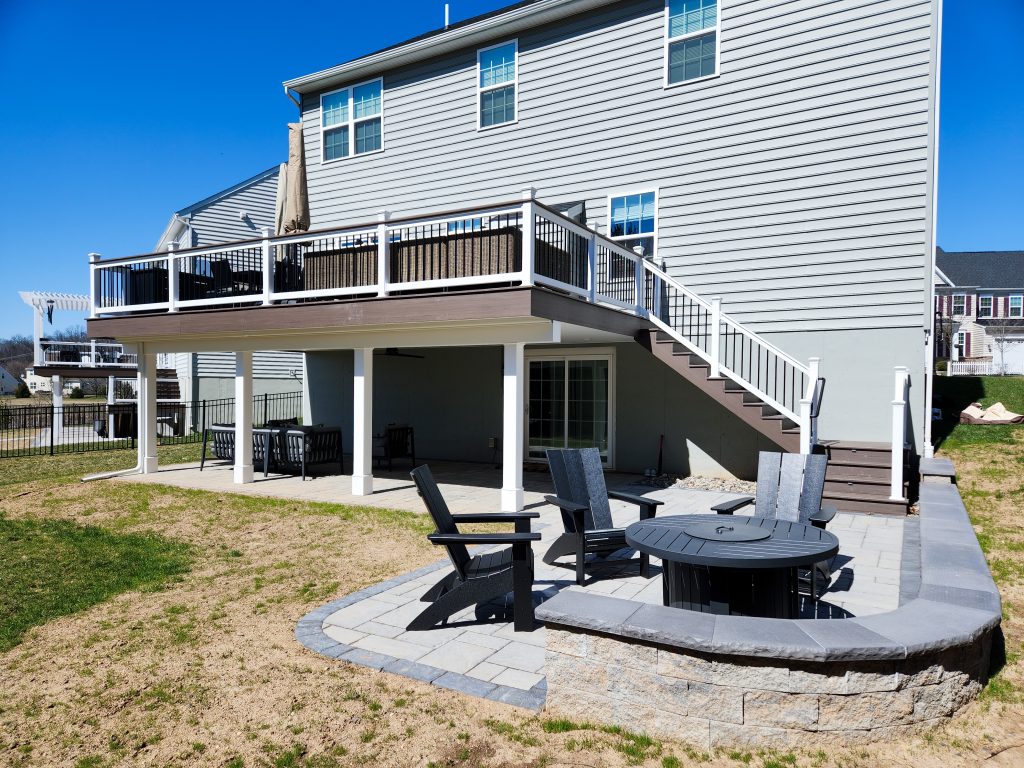 Brown deck with white railings, white posts and beams, and 2 lower patios with a close up on Adirondack chairs around a black fire pit.