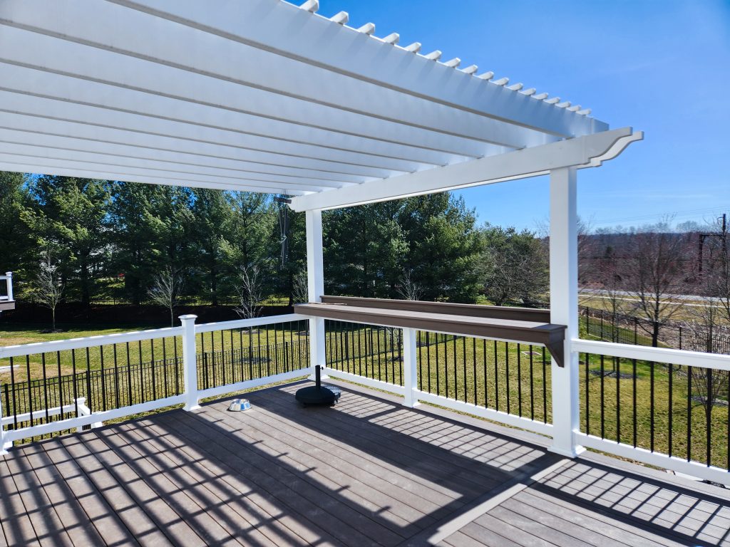 Close up of a white vinyl pergola and brown bar top on a brown deck with white railings.
