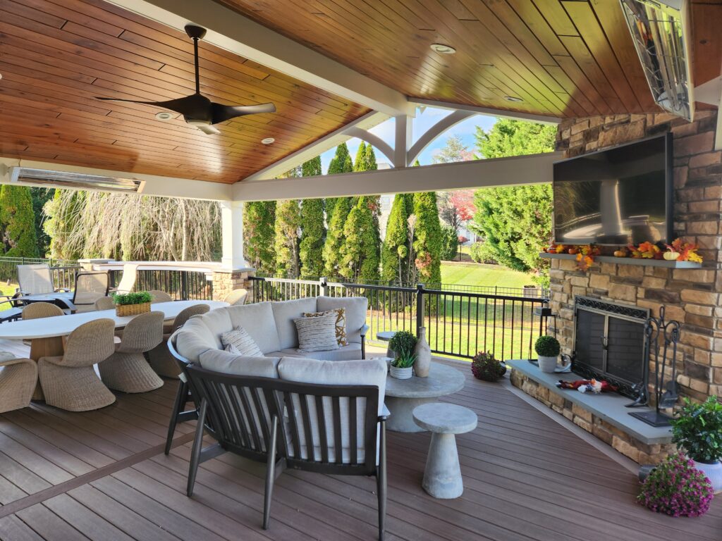 under covered roof of a deck with dining table, sofa, and tv